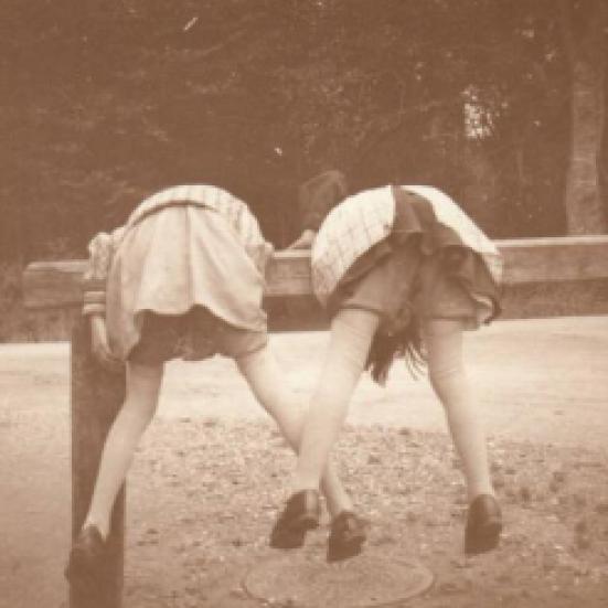 Billedet forestiller to piger, der klatre på den bom, der var  udenfor Louis Kettners forretning til at tøjre heste ved. 